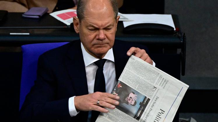 German Chancellor Olaf Scholz folds a newspaper bearing a picture of Ukraine&apos;s President Volodymyr Zelensky on it during a plenary session of the Bundestag (lower house of parliament) focusing on the budget, on November 22, 2022 in Berlin. (Photo by John MACDOUGALL / AFP)