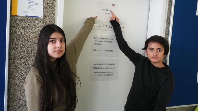Havin (links) und Burak deuten auf die englische Bezeichnung für das Sekretariat der Schule, ein Raum, der von Schülern oft aufgesucht wird. Allerdings auch von Eltern.