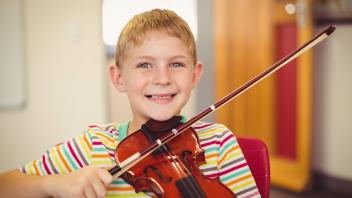 Portrait of smiling schoolboy playing violin in classroom Portrait of smiling schoolboy playing violin in classroom at s