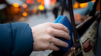 Eine Hand zieht ein Portemonnaie aus einer Handtasche. Thema Taschendiebstahl auf Weihnachtsmarkt, Themenbild, Symbolbil