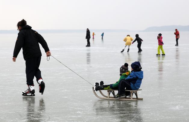 Spaziergänger und Schlittschuhläufer sind auf einem zugefrorenen See unterwegs.