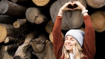 Smiling woman making heart shape in front of logs model released, Symbolfoto, HMEF01484