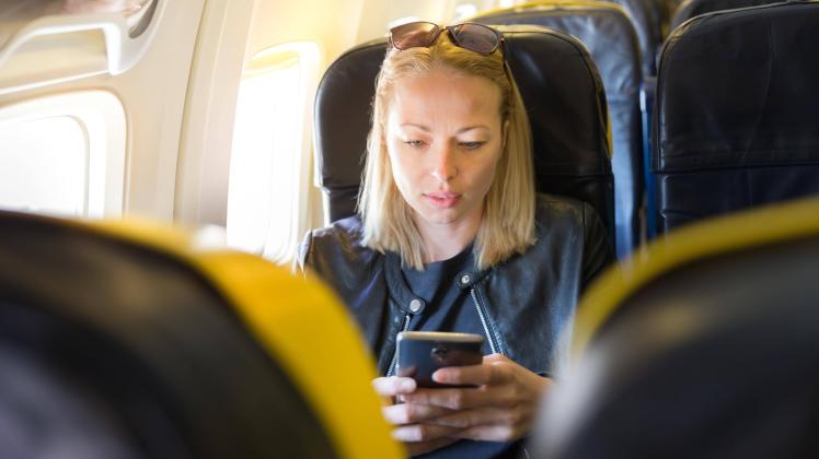 Woman using mobile phone as entertainment on airplane during commercial flight model released Sy