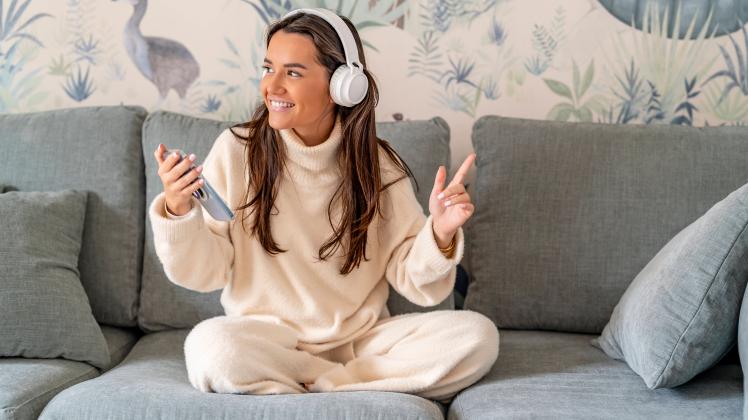 Happy woman wearing wireless headphones listening music on sofa at home model released, Symbolfoto property released, DL
