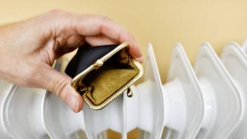 Hand hält leere Geldbörse vor einer Heizung, Symbolfoto steigende Heizkosten *** Hand holding empty purse in front of a