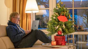 Mann arbeitet in der Weihnachtszeit gemütlich von zu Hause, Maske hängt dabei am Christbaum, München, Dezember 2022 Deut