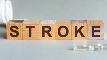 Stroke text on wooden blocks. In front of a row of cubes are ampoules, in the background - white plastic packaging from tablets, the cubes are located on a gray surface.