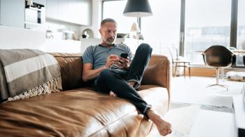 handsome bearded midaged man looking at mobile phone on sofa