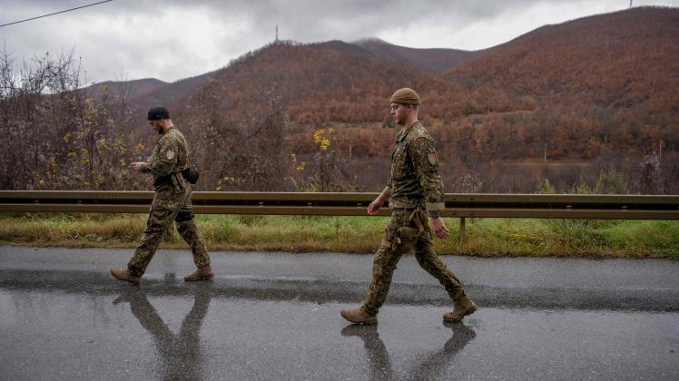 NATO soldiers serving in the peacekeeping mission in Kosovo (KFOR) walk as they inspect a road barricade set up by ethnic Serbs near the town of Zubin Potok on December 11, 2022. - Hundreds of ethnic Serbs erected barricades on a road in northern Kosovo on Saturday, blocking the traffic over the two main border crossings towards Serbia, police said. Trucks, ambulance cars and agricultural machines were used as roadblocks, heightening recent tensions which included explosions, shootings and an armed attack on a police patrol which saw one ethnic Albanian police officer wounded. (Photo by Armend NIMANI / AFP)