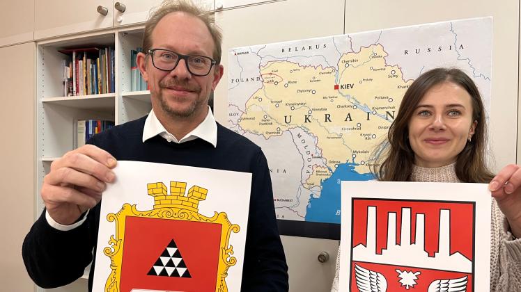 Stadtmitarbeiterin Marta Melnik ist in der Ukraine geboren und stellte den Kontakt nach Novovolynsk her.  Oberbürgermeister Tobias Bergmann hält das Wappen der ukrainischen Stadt.