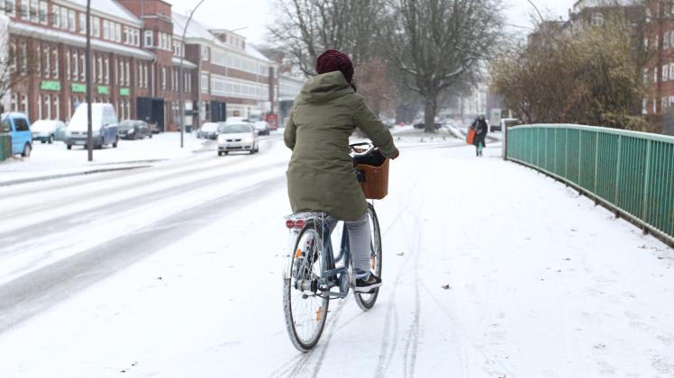 Eine Fahrradfahrerin fährt während des Schneefalls am Donnerstagmittag in Hamburg auf einem schneebedecktem Fahrradweg.