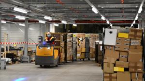 Ein Mitarbeiter transportiert Sendungen in mehreren Rollbehältern quer durch das Paketzentrum.