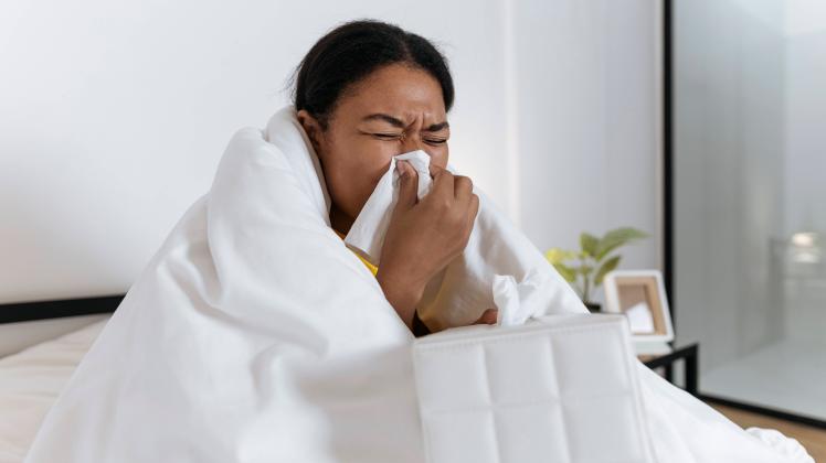 Sick woman sitting on bed wrapped in a blanket blowing nose in a tissue model released, Symbolfoto property released, SI