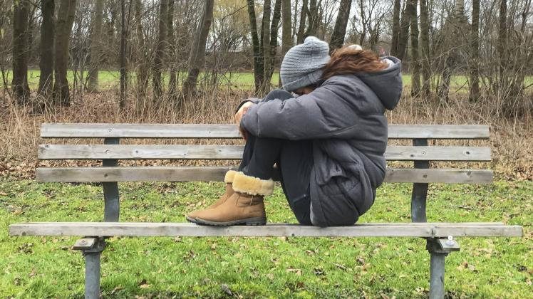 Junge Frau traurig und enttaeuscht auf einer Parkbank im Wald sitzend am 01 02 2016 in Muenchen Deu