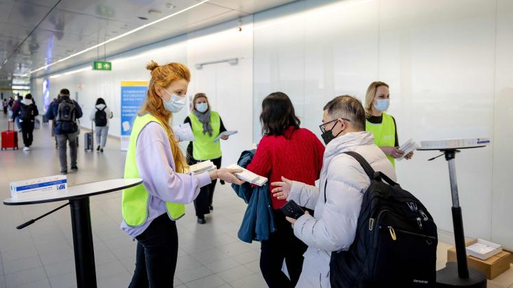 An employee of the the Dutch Municipal Health Service (GGD) hands out free Covid-19 self-test kits to travelers arriving from China, at Amsterdam's Schiphol Airport on January 4, 2023. - More than a dozen countries have imposed coronavirus testing requirements on visitors from China, which is experiencing an explosion of cases after lifting its long-standing zero-Covid measures. (Photo by Robin van Lonkhuijsen / ANP / AFP) / Netherlands OUT