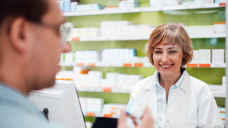 Smiling female pharmacist looking at customer checking medicine model released Symbolfoto property released JOSEF05416