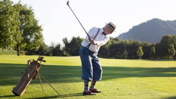 Älterer Mann mit Strohhut und Knickerbocker spielt Hickory Golf auf einem Golfplatz *** Older man in straw hat and knick