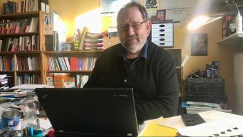 Ein Mann sitzt an einem Schreibtisch vor einem aufgeklappten Laptop.