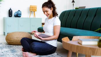 Woman smiling while reading book sitting at home model released Symbolfoto property released GIOF11054