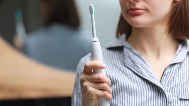 woman using electric toothbrush at home. technology and health care