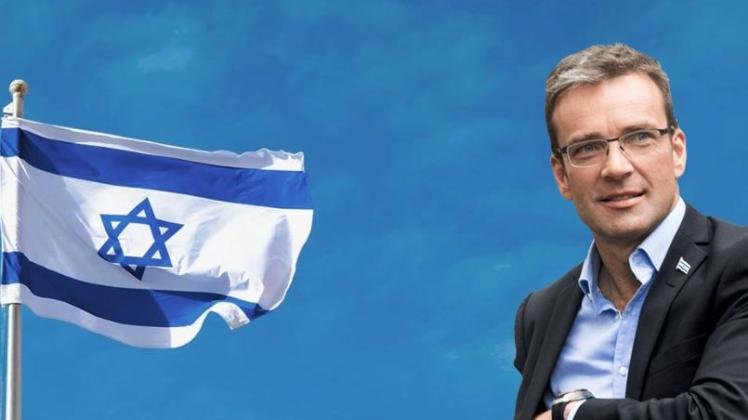 Doron Schneider vor blauem Hintergrund und mit israelischer Flagge