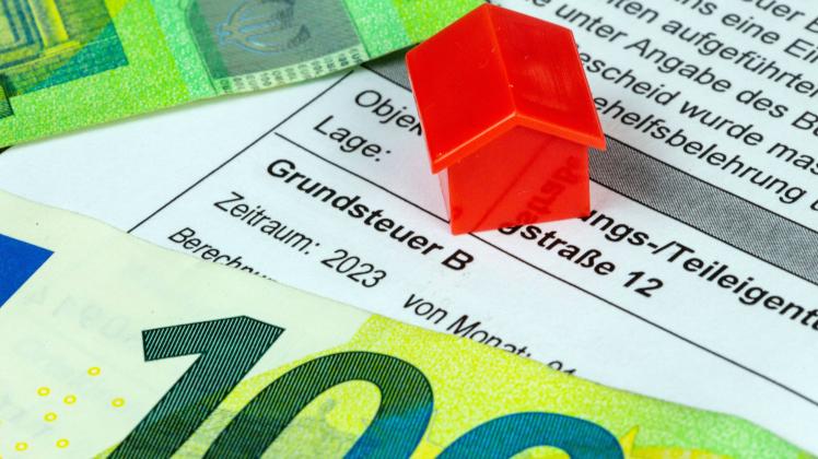 Nahaufnahme eines Bescheides über Grundbesitzabgaben mit Eurobanknoten und einem Modellhaus (Symbolbild) *** Close up of