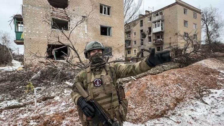 RUSSIA, DONETSK PEOPLE S REPUBLIC - JANUARY 20, 2023: A Wagner Group fighter stands before a building destroyed by heavy
