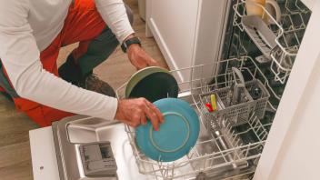 Mann im weißen T-Shirt räumt in der Küche seines Hauses das Geschirr in die Spülmaschine *** Man at white T Shirt clears