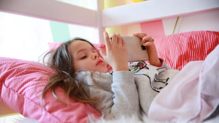 Ein Kind liegt im Bett und hat ein Smartphone in der Hand