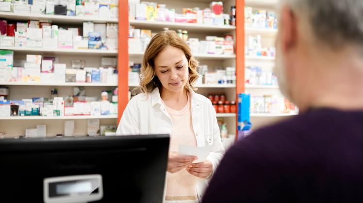 Female pharmacist reading prescription to customer at checkout counter in pharmacy store model released property releas