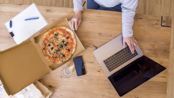 Woman at home office using laptop while eating pizza top view model released Symbolfoto property re