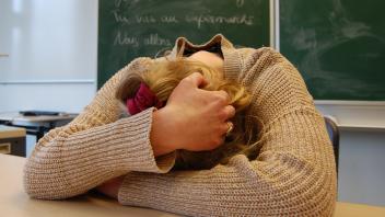 Eine Lehrerin liegt mit ihrem Oberkörper erschöpft auf dem Lehrerpult im Klassenzimmer eines Husumer Gymnasiums.