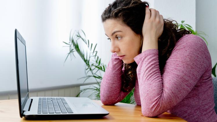 Side view of concentrated female freelancer with hands on head browsing netbook while sitting at wooden table in light r
