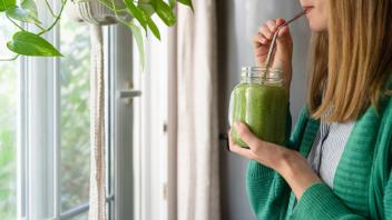 Woman drinking green smoothie standing by window at home model released, Symbolfoto property released, SVKF00937