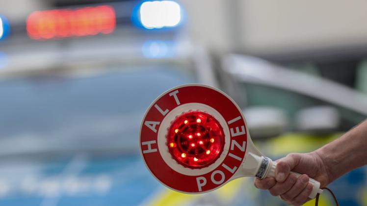 Themenbild Polizei Ein Polizist hält eine Kelle mit der Aufschrift Halt Polizei vor einem Streifenwagen in die Luft, das