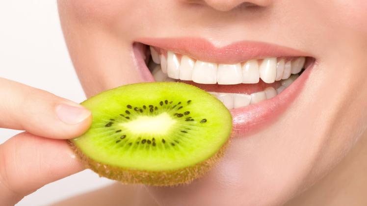 Beautiful female mouth with big teeth holds kiwi slice in front of her lip model released Symbolf
