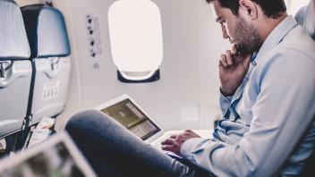 Businessman working with laptop on airplane. Casually dressed middle aged man working on laptop in aircraft cabin during