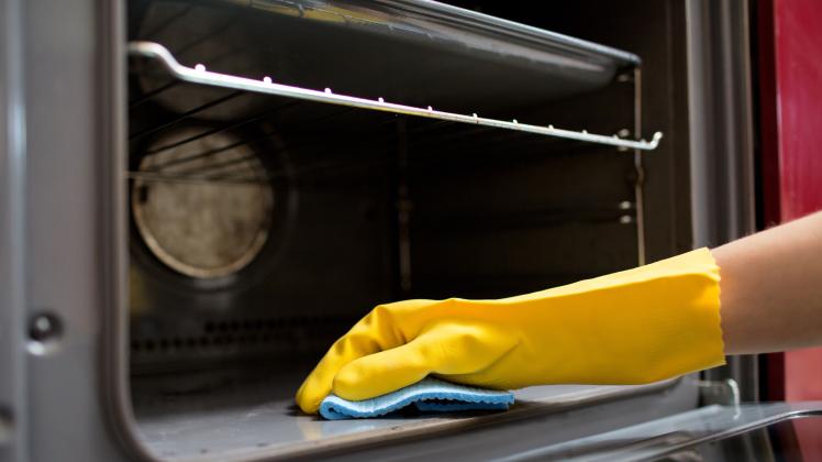 people, housework and housekeeping concept - hand in rubber glove with rag cleaning oven at home kitchen (dolgachov)