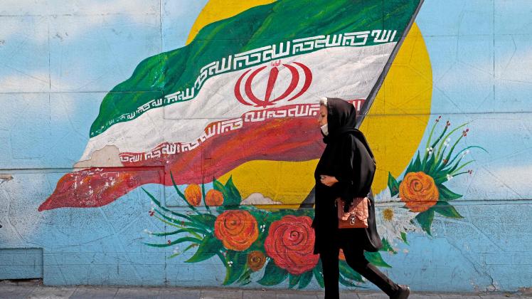(FILES) In this file photo taken on October 11, 2022, a woman walks past a mural in the Iranian capital Tehran. - Iran's parliament and the judiciary are reviewing a law which requires women to cover their heads, and which triggered more than two months of deadly protests, the attorney general said on December 3, 2022. (Photo by ATTA KENARE / AFP)