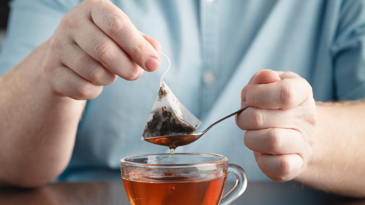 Teabag in the cup with hot water in hands (AndreyCherkasov)
