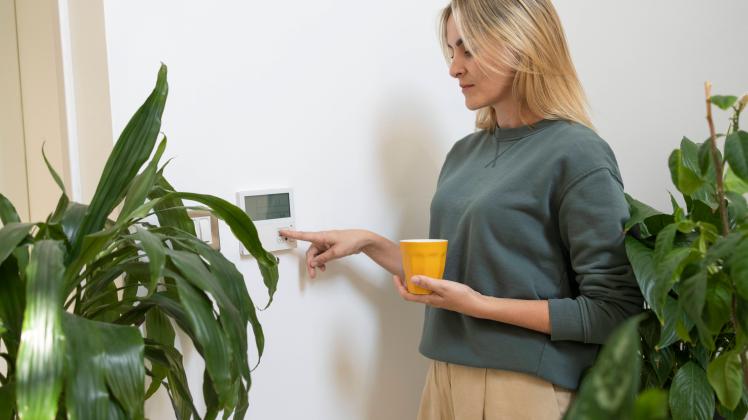 Woman with coffee cup adjusting smart thermostat at home model released, Symbolfoto property released, SVKF01157