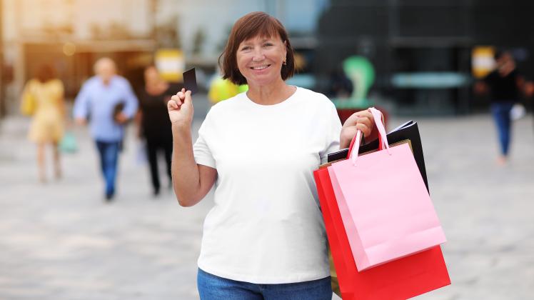 Smiling stylish middle aged woman with credit, debit card and shopping bags standing on shopping mall background. Autumn holidays, discounts, black Friday. concept of consumerism, sale, rich life