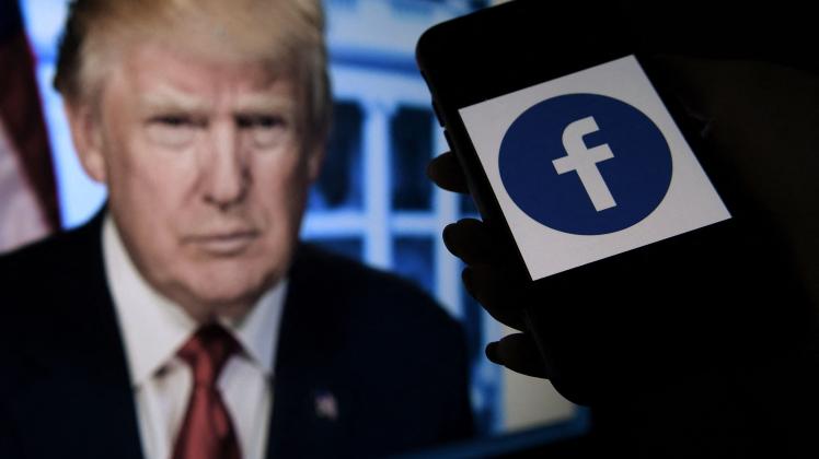 (FILES) In this file illustration photo taken on May 4, 2021, a phone screen displays a Facebook logo with the official portrait of former US President Donald Trump on the background in Arlington, Virginia. - Social networking giant Meta announced Wednesday January 25 that it would, in the coming weeks, "end the suspension" of Donald Trump's Facebook and Instagram accounts, two years after the former U.S. president was banned following the assault on the Capitol. (Photo by Olivier DOULIERY / AFP)