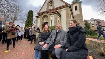 Bischof Franz-Josef Bode nimmt während der Jubiläumsfeier in Icker auf der neuen „Dorfblick“-Bank Platz, die die Jugend zum 100-jährigen Bestehen der Kirche gestiftet hatte, hier mit Malin Thünemann (links) und Sophie Glandorf.