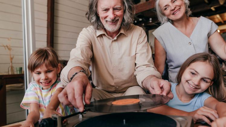 Smiling grandfather changing record on turntable by granddaughters at home model released, Symbolfoto property released,