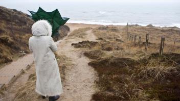 Frau steht mit einem Schirm im Sturm am roten Kliff, Kampen, Sylt, nordfriesische Insel, Schleswig-Holstein, Deutschland, Europa