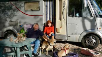 Zwei erfahrene Camper mit Hunden vor ihrem Wohnmobil                              