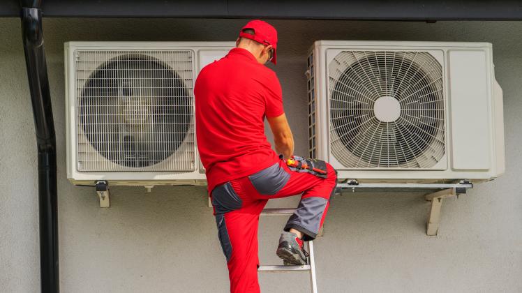 EIn Techniker montiert eine Wärmepumpe an eine Hausfassade 