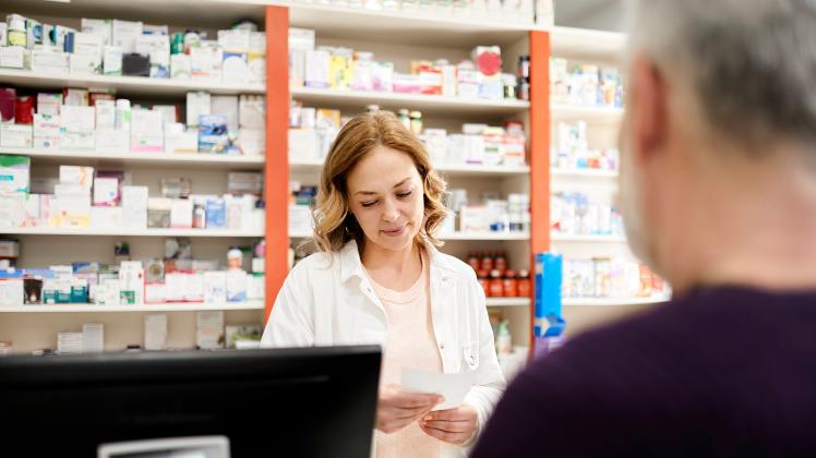 Female pharmacist reading prescription to customer at checkout counter in pharmacy store model released property releas