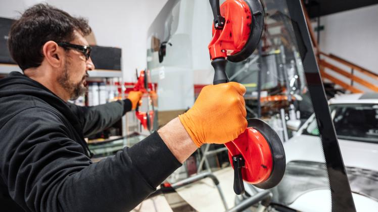 Automobile technician worker replacing windscreen or windshield of a car in auto service station garage. Automobile tech